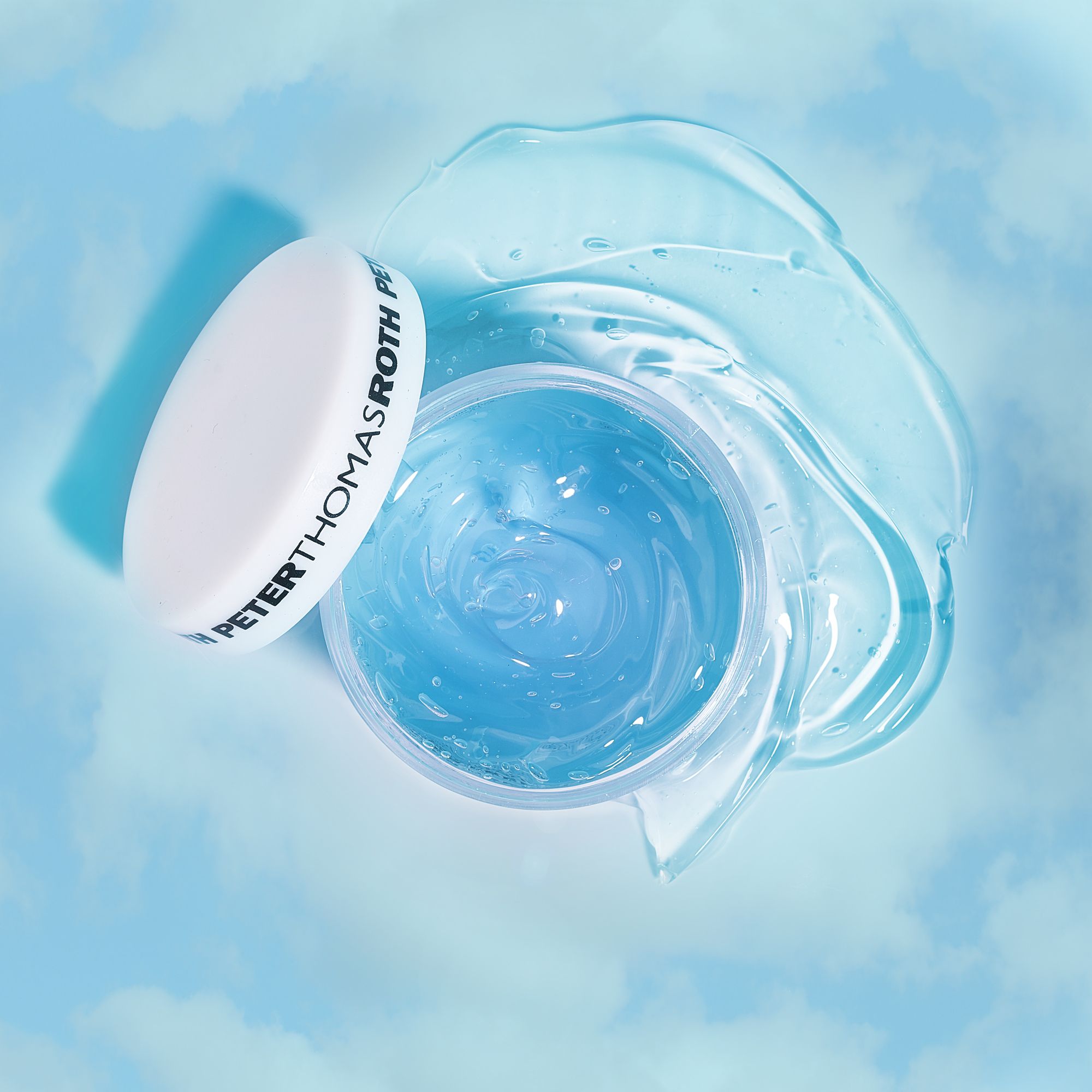 Vasetto blu aperto con coperchio bianco. Gel accanto. Scritta: Peter Thomas Roth. Sfondo: cielo blu con nuvole.