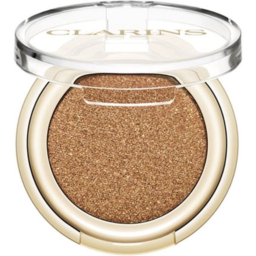 Contenitore rotondo di ombretto con bordo dorato e coperchio trasparente. Ombretto marrone glitterato. Scritta Clarins sul coperchio.