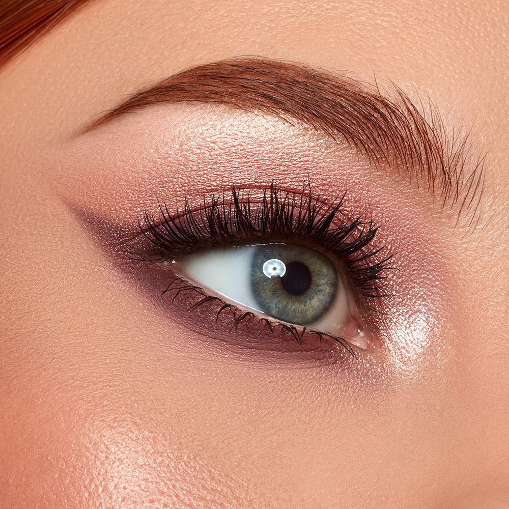 Un occhio truccato con ombretto rosa. L'ombretto è applicato sulla palpebra e sotto l'occhio. Il sopracciglio è modellato e le ciglia sono valorizzate con il mascara.