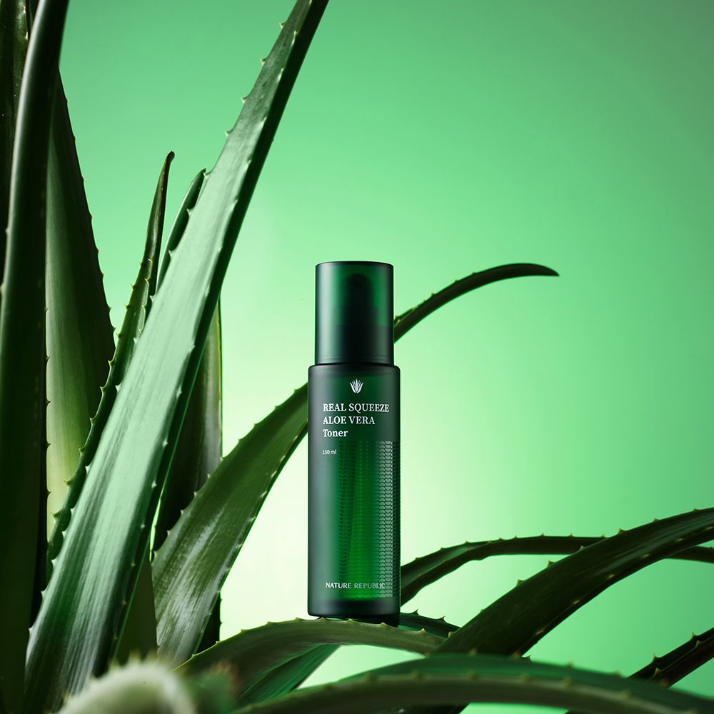 Flacone verde di toner all'aloe vera, circondato da foglie di aloe vera su sfondo verde.