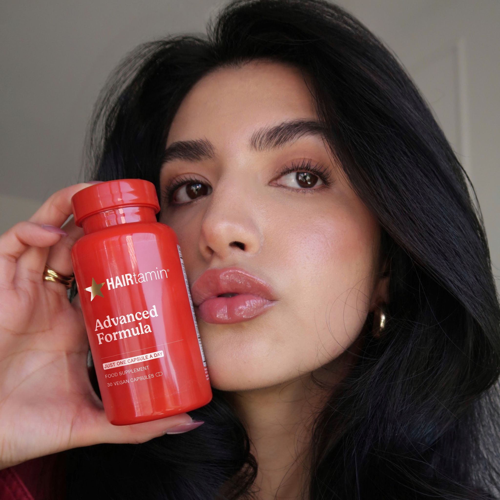 Flacone rosso HAIRtamin Advanced Formula. Donna che tiene il flacone. Scritta: Advanced Formula.