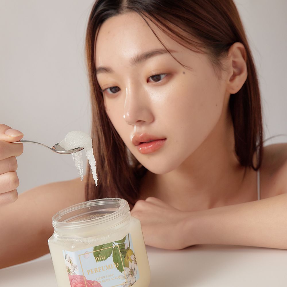 Donna tiene cucchiaio con prodotto. Vaso con coperchio dorato ed etichetta floreale. Prodotto visibile.