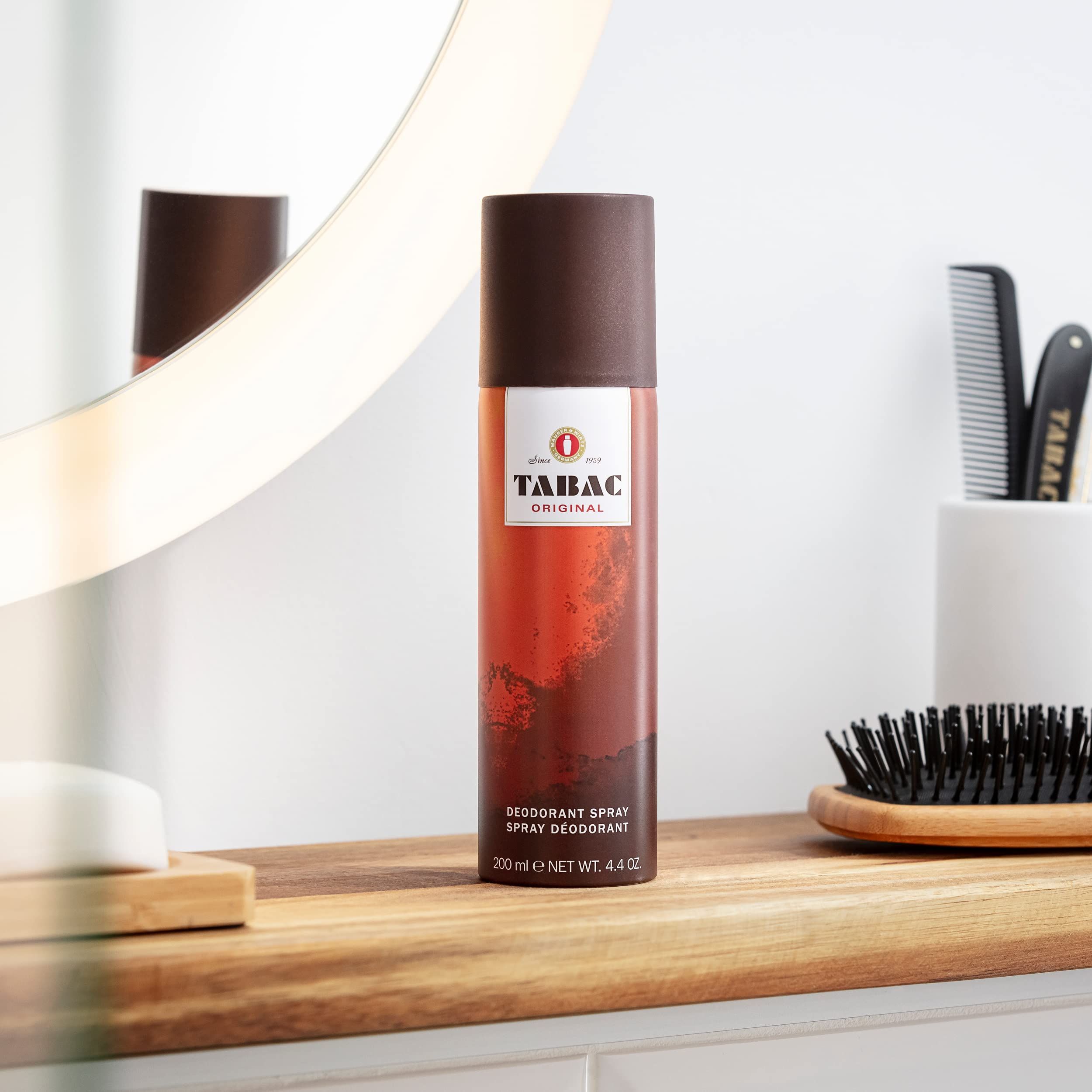 Spray deodorante su ripiano in legno. Tappo marrone, etichetta con TABAC ORIGINAL. In background: specchio, pettine, sapone.