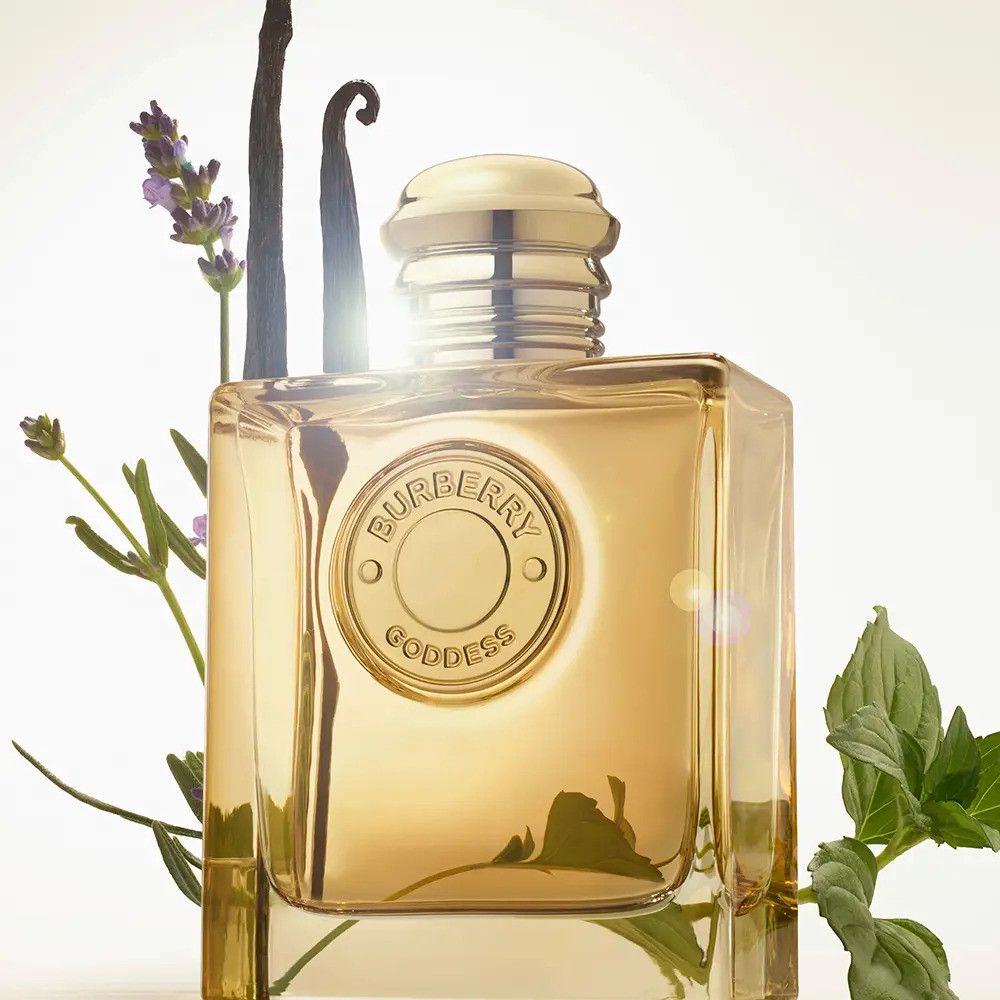 Flacone dorato con tappo dorato, circondato da piante. Scritta Burberry Goddess.
