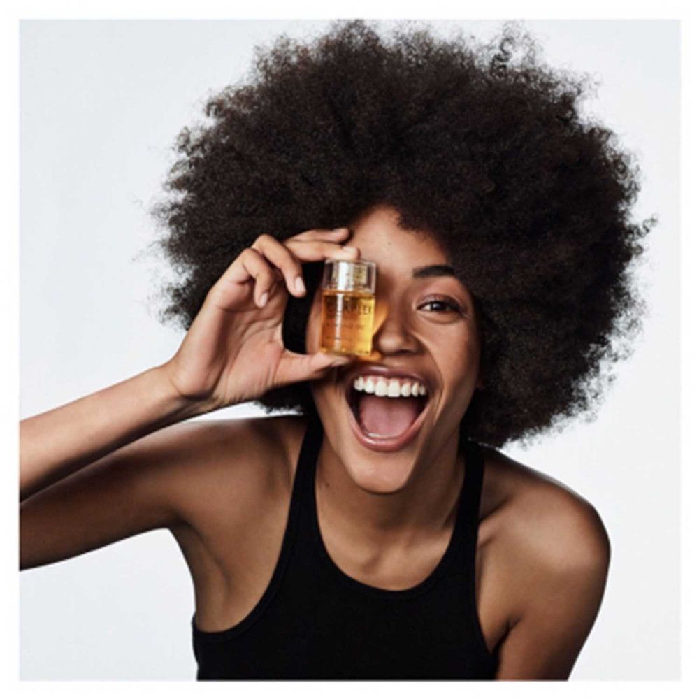 Donna tiene Olaplex No.7 Bonding Oil davanti all'occhio. Sorride. Scritta: Olaplex No.7 Bonding Oil.