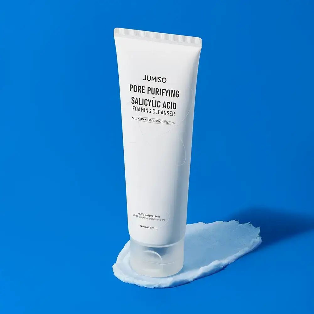 Tubo bianco con prodotto. Scritta: JUMISO Pore Purifying Salicylic Acid Foaming Cleanser. Su sfondo blu con prodotto.