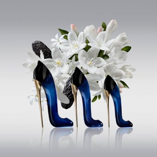 Tre flaconi neri a forma di scarpa con tacco dorato. Liquido blu visibile. Fiori bianchi sullo sfondo.