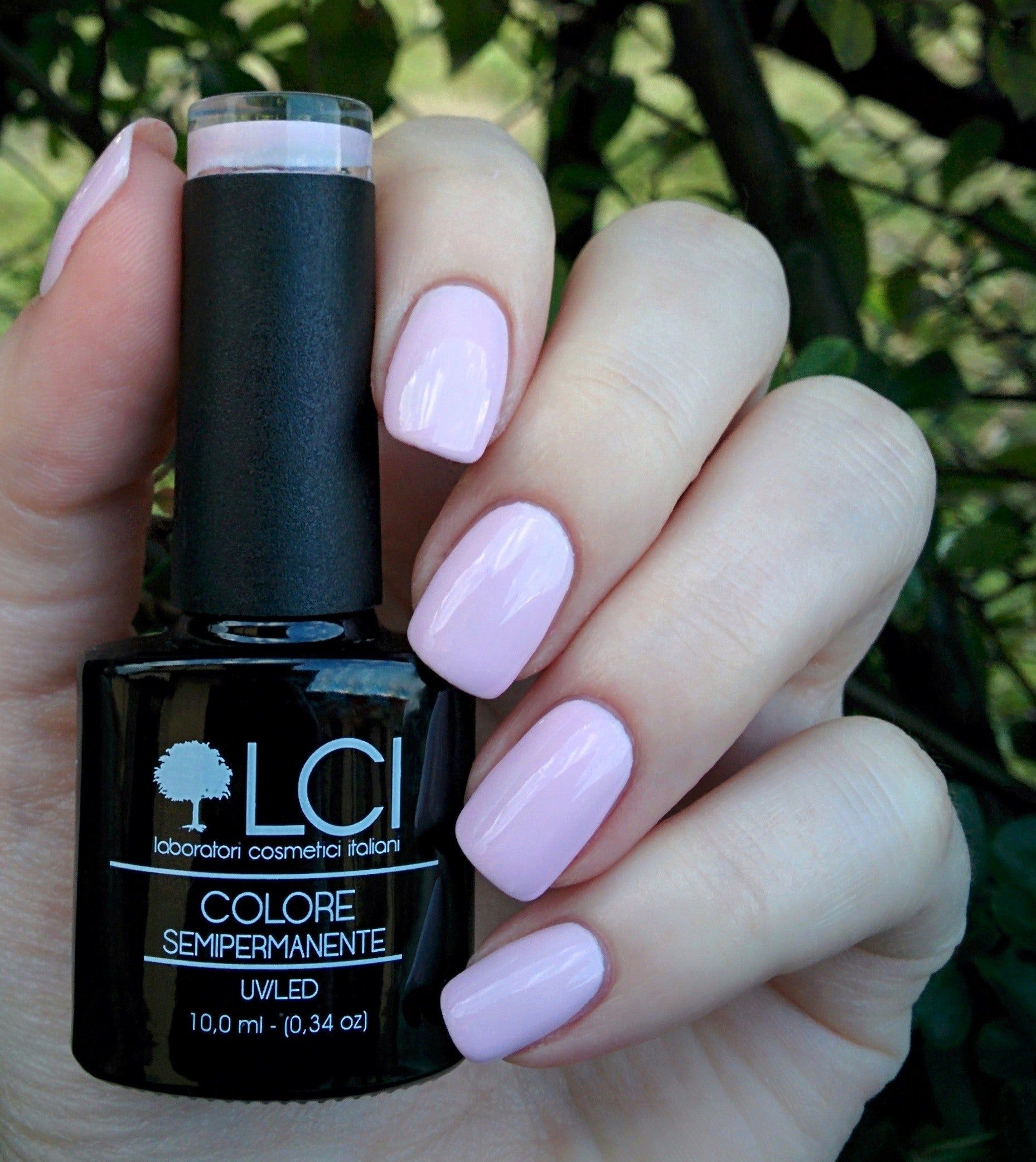 Mano con unghie smaltate e flacone di smalto. Unghie smaltate di rosa. Flacone di smalto nero con testo bianco.