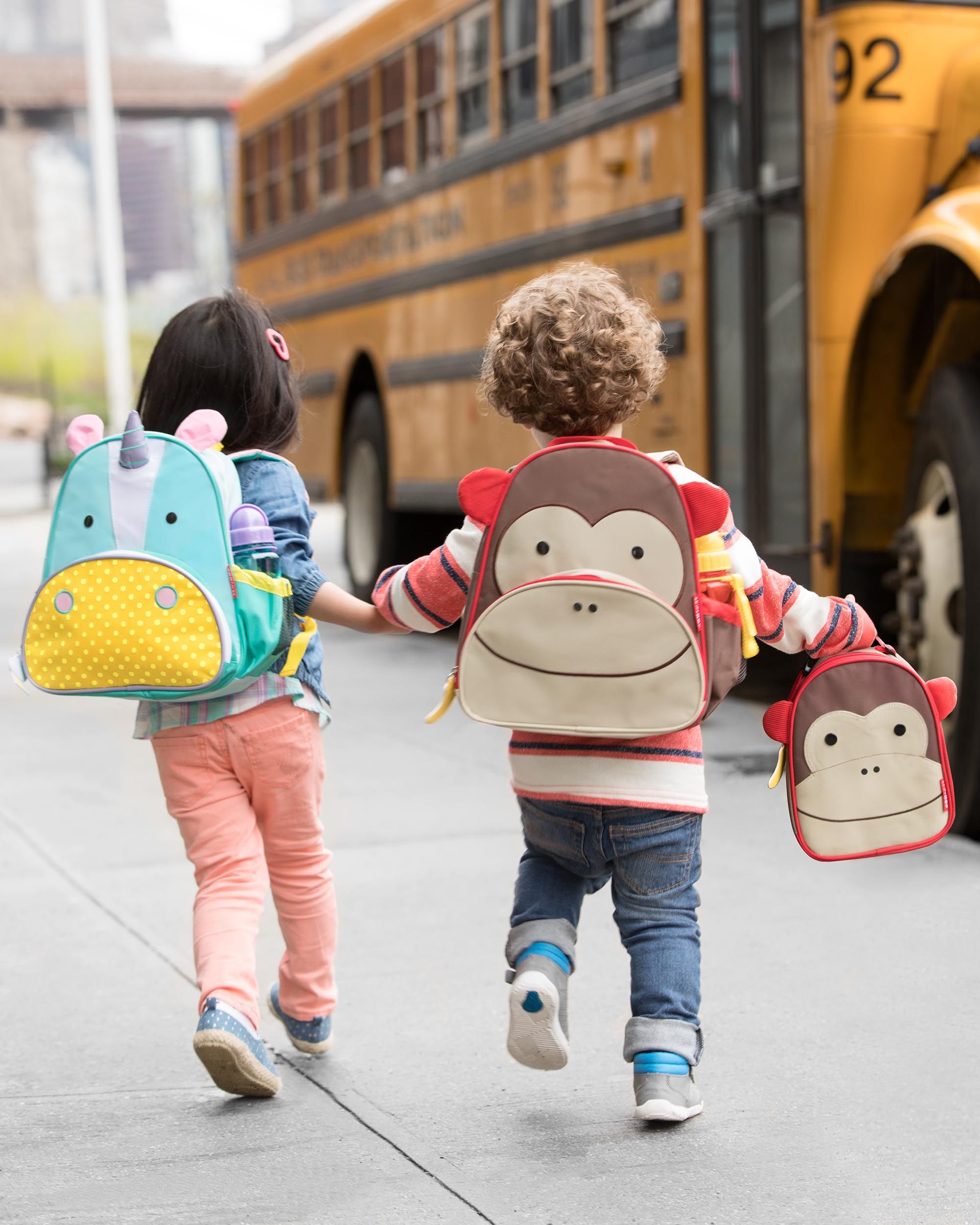 Due bambini vanno a scuola con zaini. Uno con zaino unicorno, l'altro con zaino scimmia.