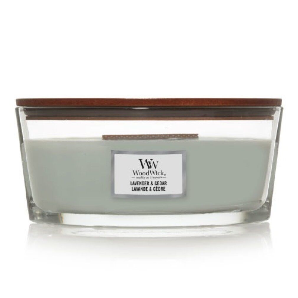 Candela con coperchio in legno. Scritta: WoodWick, Lavanda & Cedro. Contenitore in vetro, cera grigio chiaro.