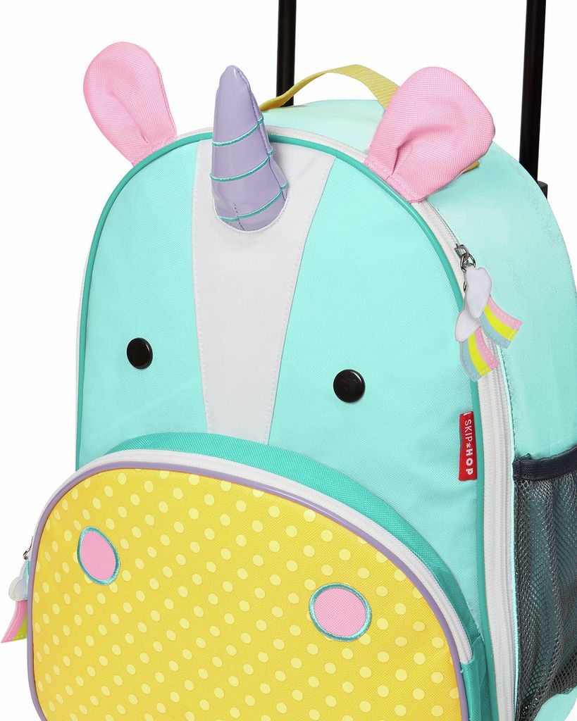 Primo piano della valigia per bambini turchese con design unicorno. Orecchie rosa, corno viola, occhi neri. Cerniera con ciondolo arcobaleno.