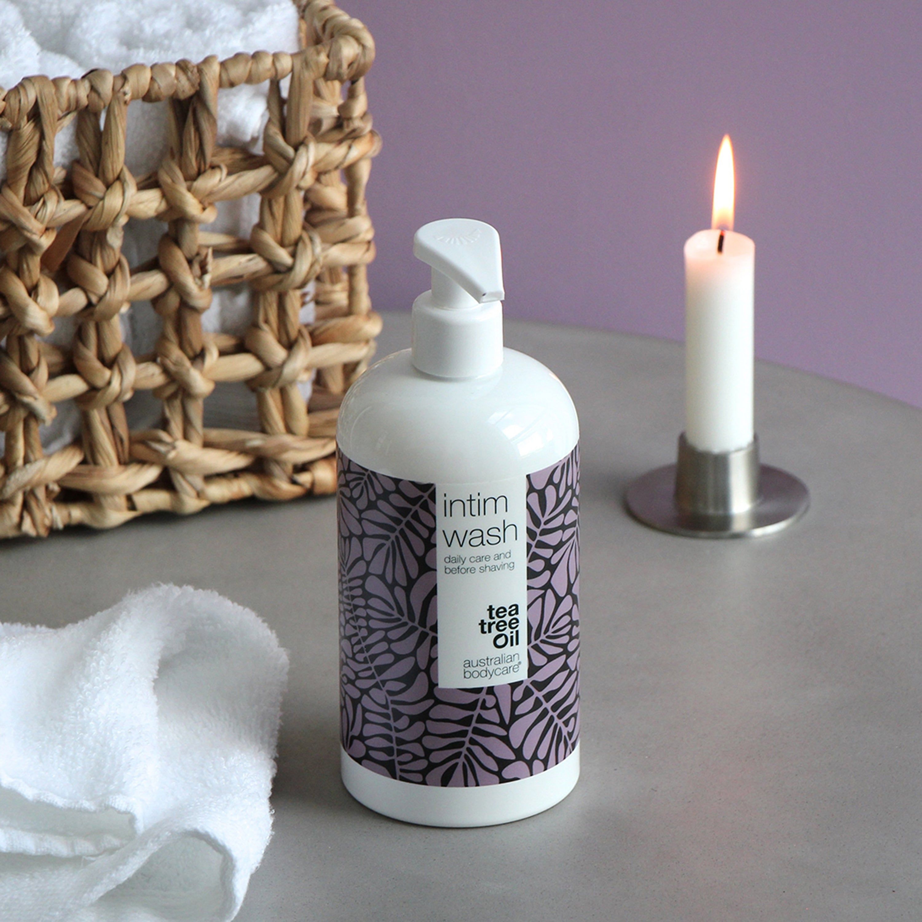 Flacone bianco di detergente intimo. Motivo a foglie viola. Scritta: Intim Wash, daily care & before shaving, Australian Bodycare. Candela.