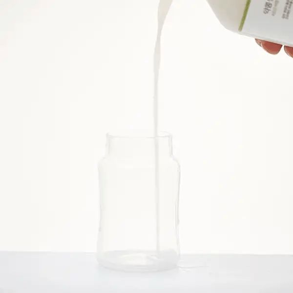 Liquido versato da una bottiglia in un bicchiere vuoto. Sfondo bianco. Primo piano.