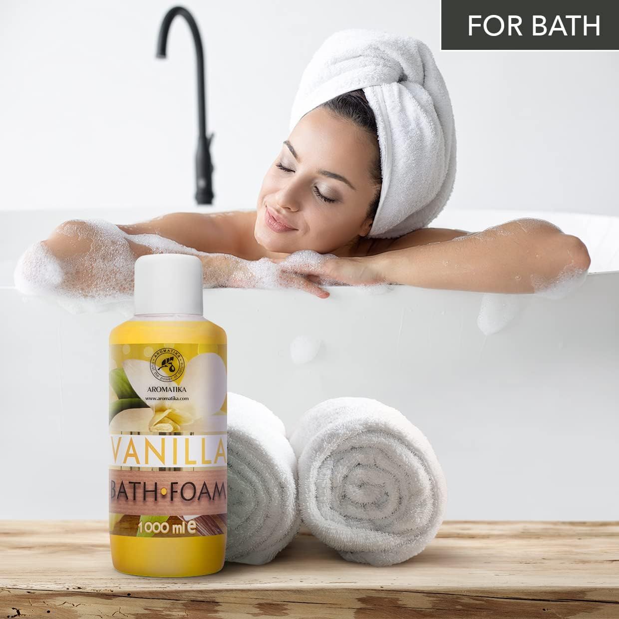 Bottiglia gialla con tappo bianco accanto a una donna nella vasca da bagno. Scritta: AROMATIKA, VANILLA BATH FOAM. Asciugamani.