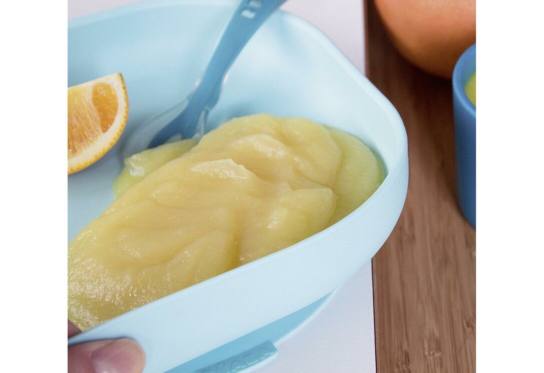 Piatto per bambini azzurro con pappa e cucchiaio. Fetta di limone. Su fondo in legno.