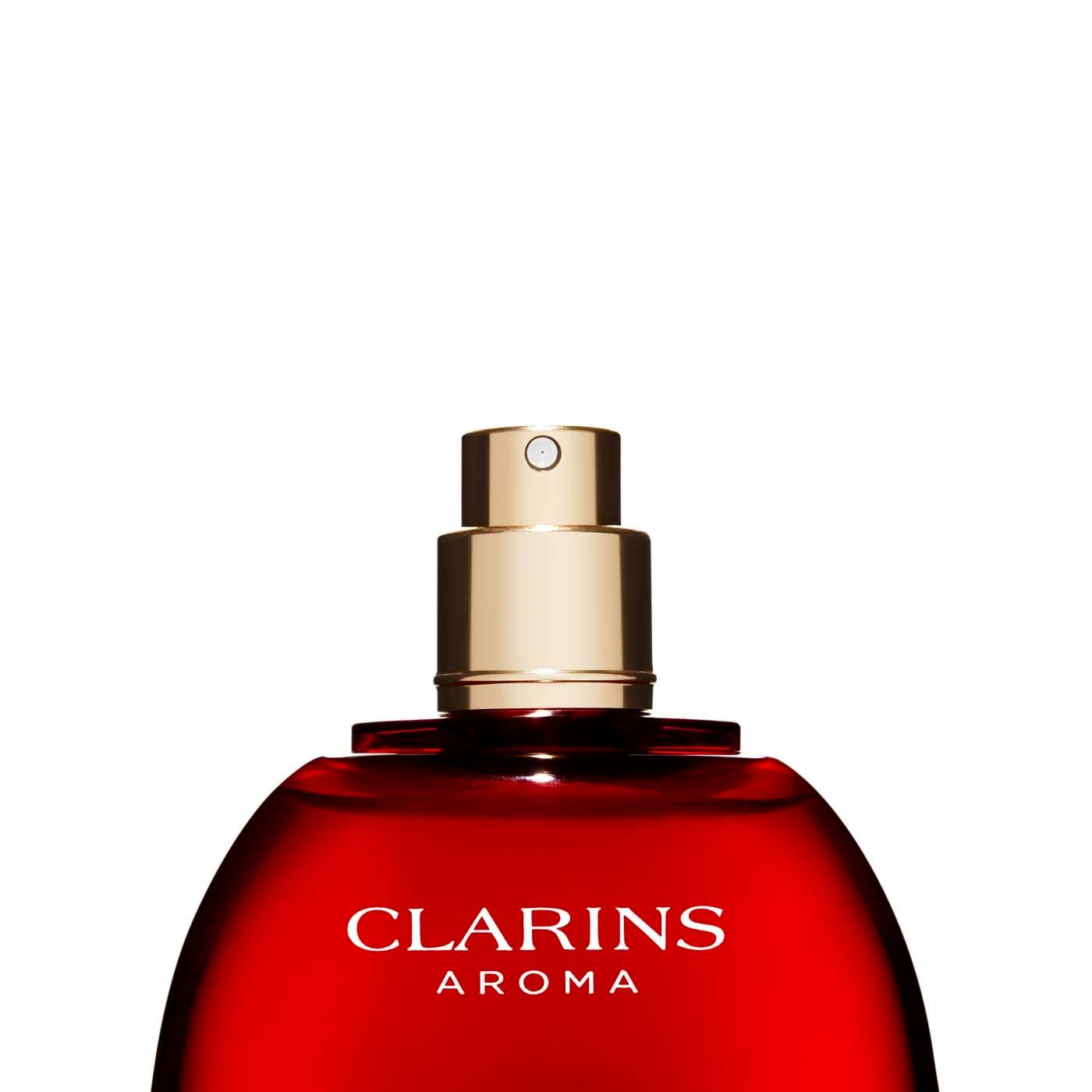 Primo piano del flacone rosso Clarins Aroma. Testina spray dorata. Tappo bianco. Su sfondo bianco.