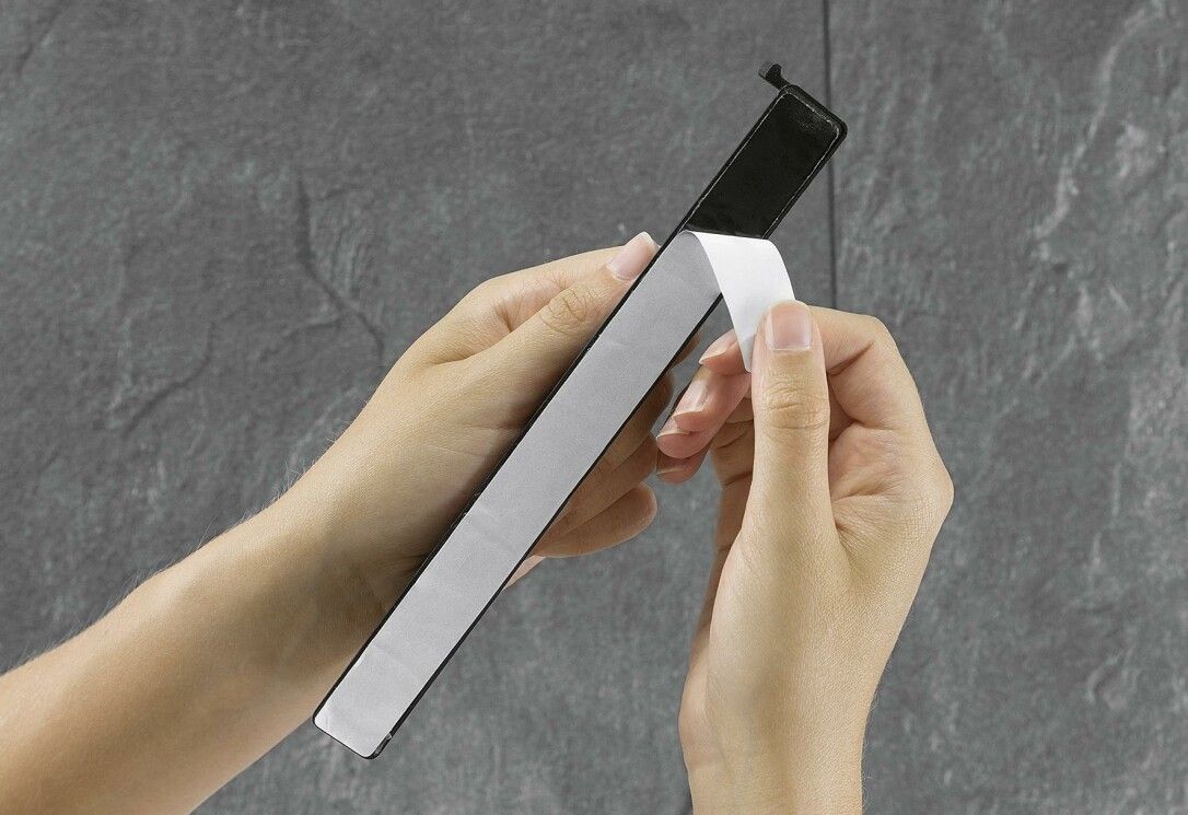 Persona che tiene una protezione per piano cottura con strisce adesive. Parte in plastica nera con nastro adesivo bianco.