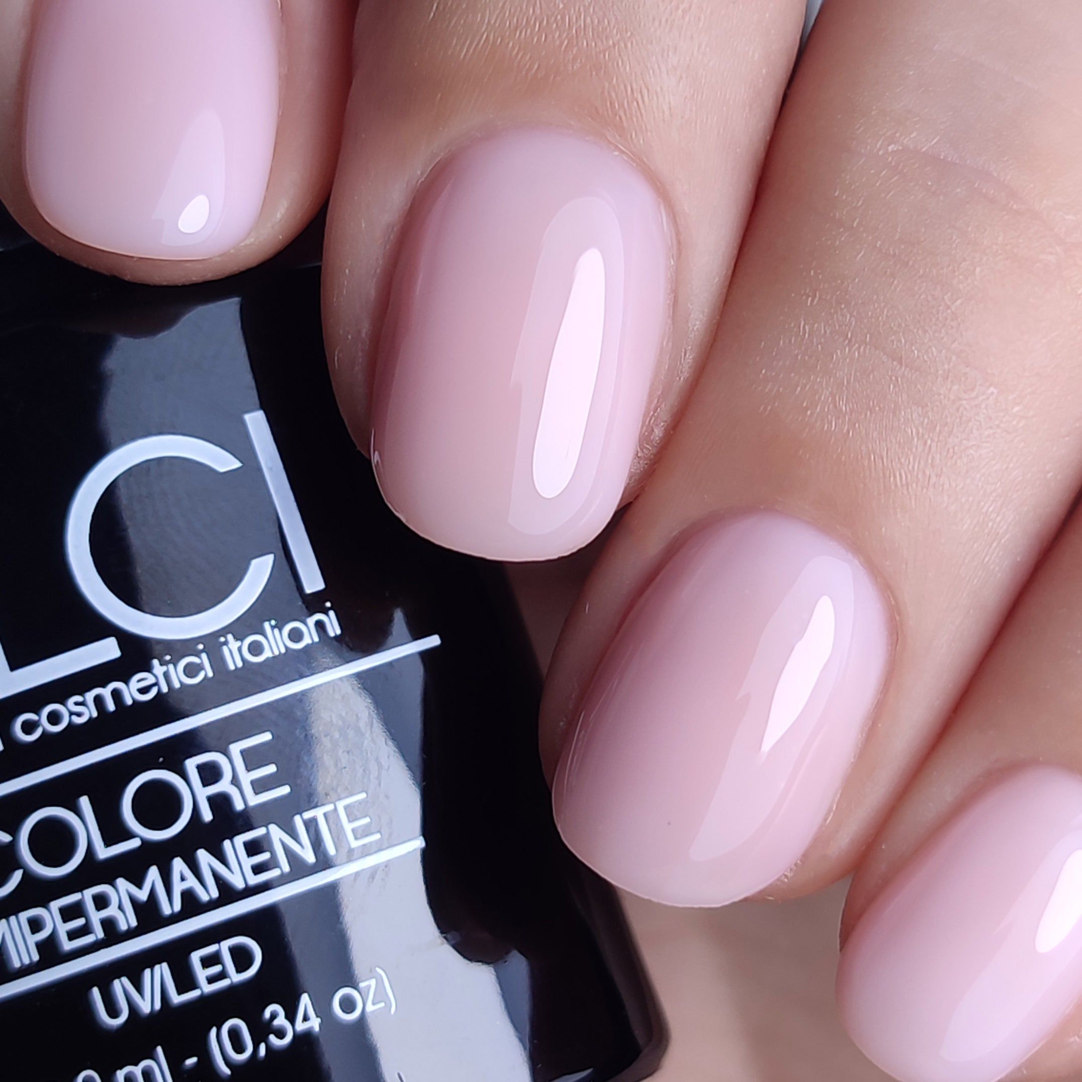 Mano con unghie smaltate rosa chiaro. Flacone di smalto parzialmente visibile con scritta: LCI, Colore Semipermanente.