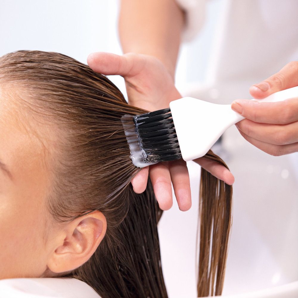 Persona che applica il balsamo sui capelli bagnati con un pennello. Primo piano. Ambiente luminoso.