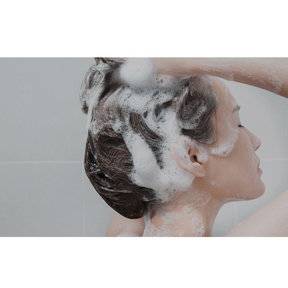 Persona che si lava i capelli con lo shampoo. La schiuma copre i capelli.