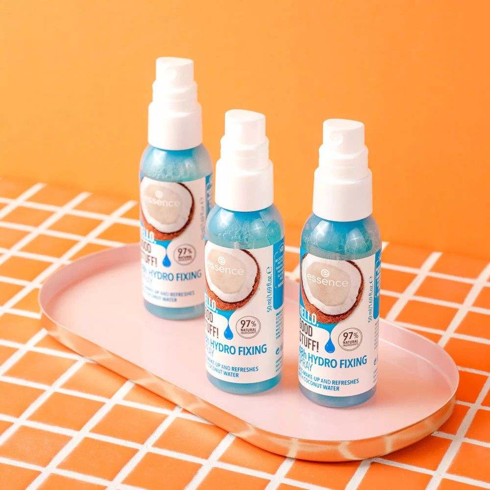 Tre flaconi spray su un vassoio. Scritta: Hello Good Stuff, 48h Hydro Fixing Spray. Con acqua di cocco. Sfondo: arancione.