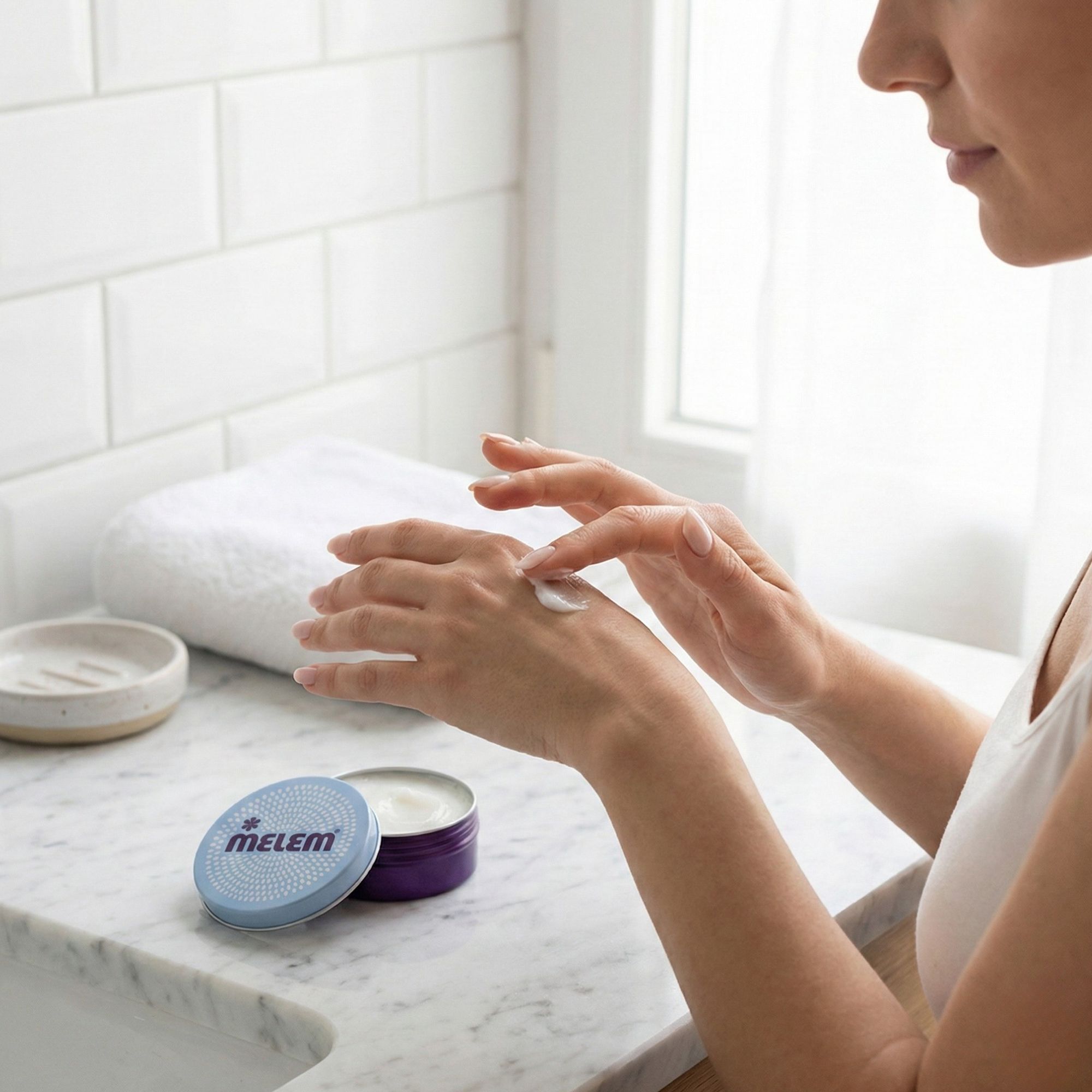 Persona che applica la crema. Barattolo rotondo aperto con logo "MELEM". Barattolo accanto a persona che applica crema sulla mano.