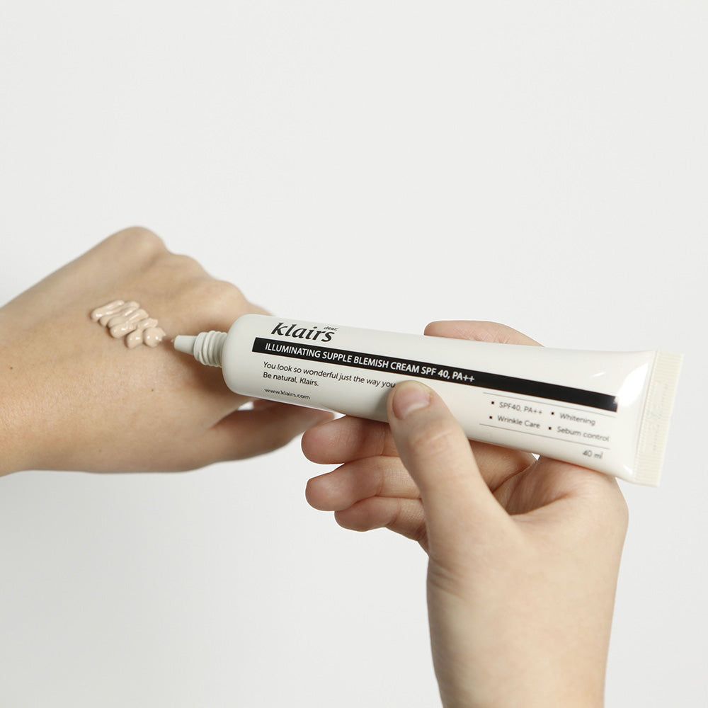 Mani che tengono un tubetto. Crema applicata sulla pelle. Scritta: Dear Klairs Illuminating Supple Blemish Cream SPF 40.