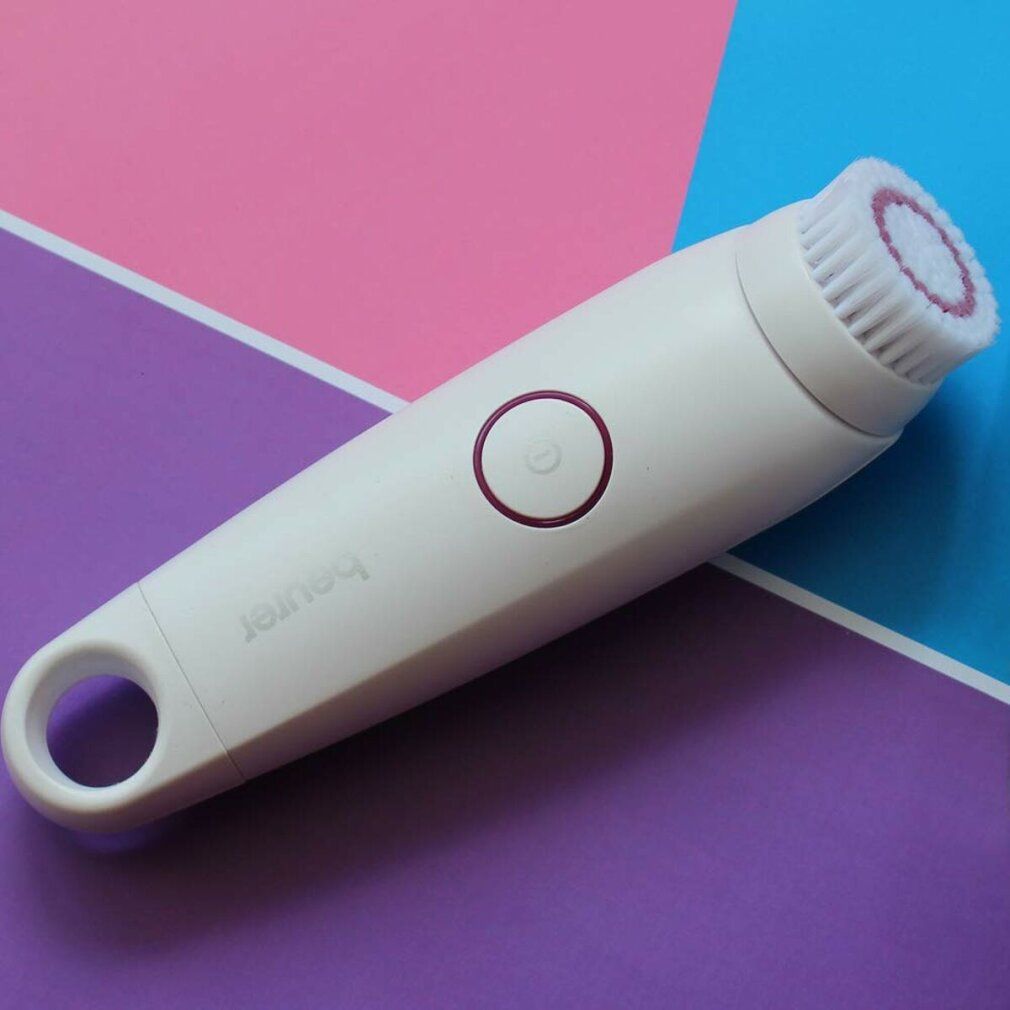Dispositivo di pulizia bianco ovale su sfondo colorato. Testina a spazzola, pulsante rosa, marchio "beurer". Manico con foro.