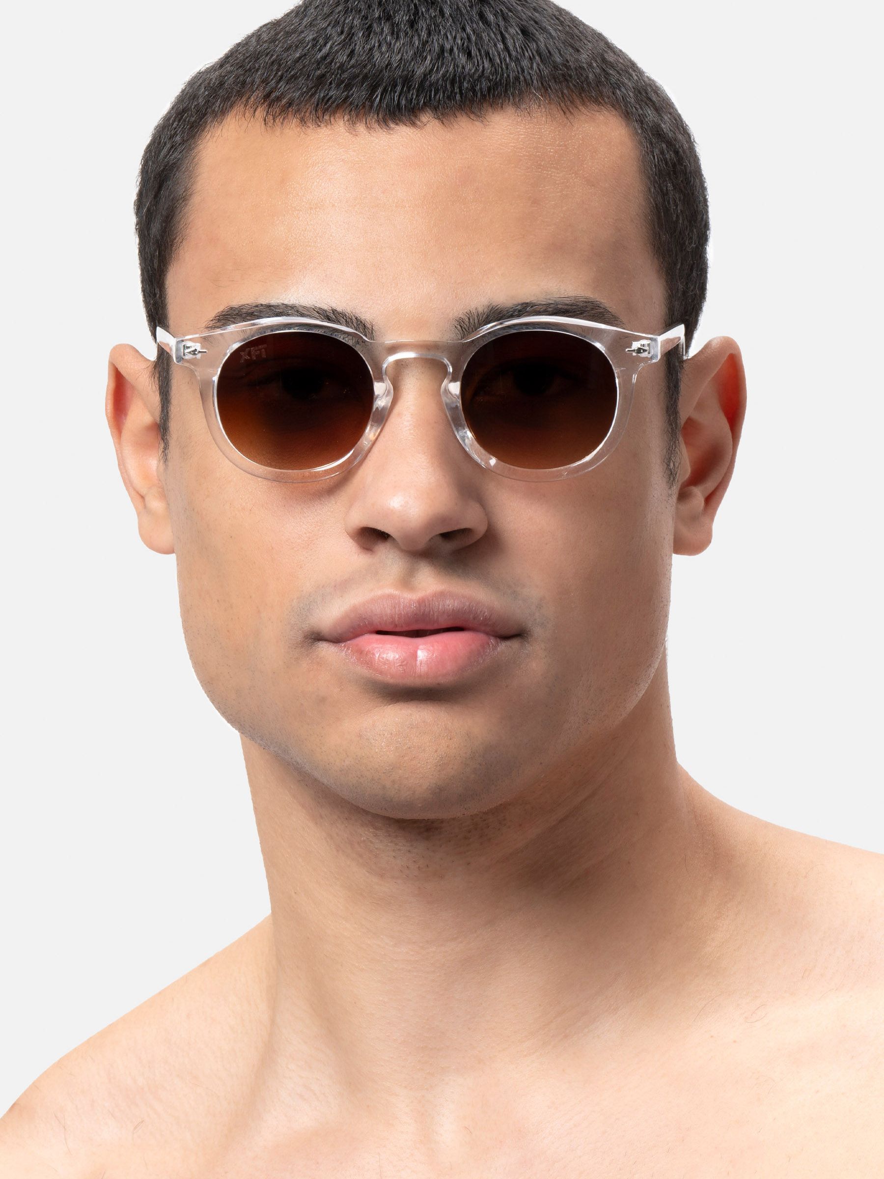 Uomo con occhiali da sole con montatura trasparente e lenti marroni. Primo piano.