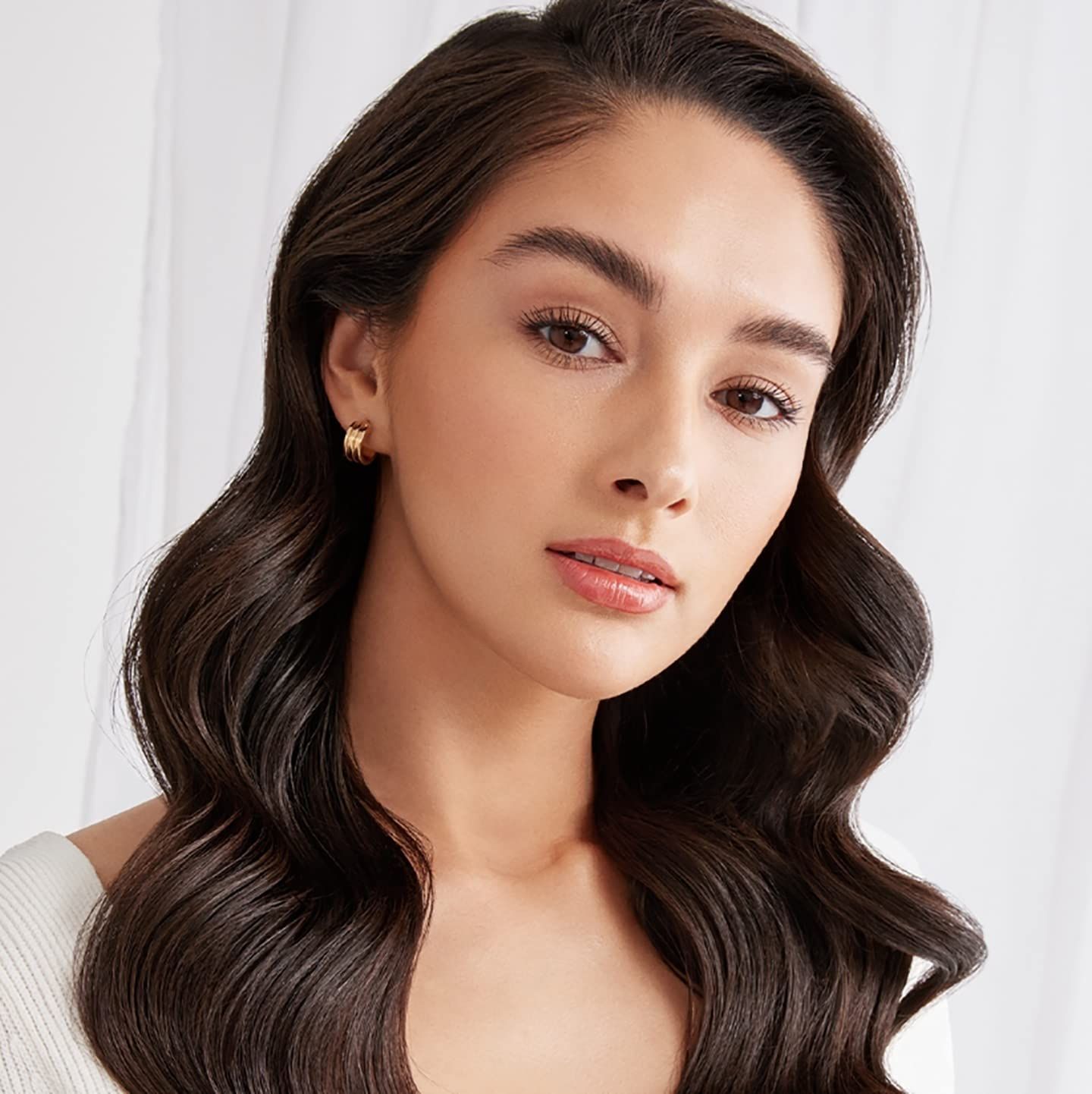 Ritratto di donna con capelli lunghi e mossi. Indossa orecchini.