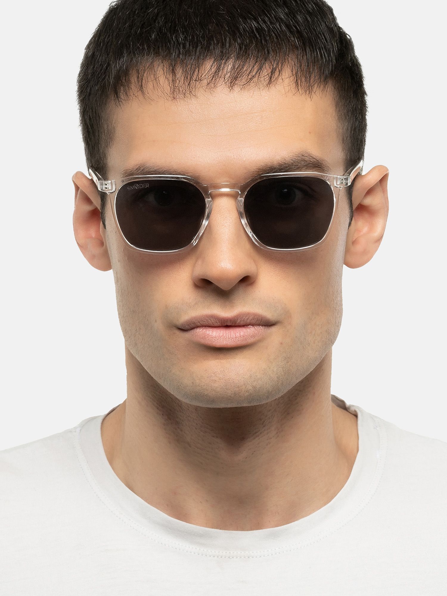 Uomo con occhiali da sole trasparenti e lenti scure. Forma quadrata, montatura trasparente. Primo piano.