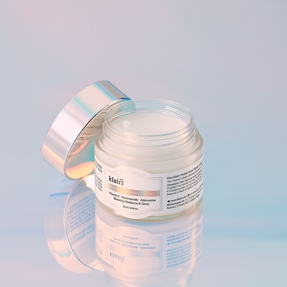 Un barattolo aperto della Freshly Juiced Vitamin E Mask con coperchio argentato su una superficie riflettente.