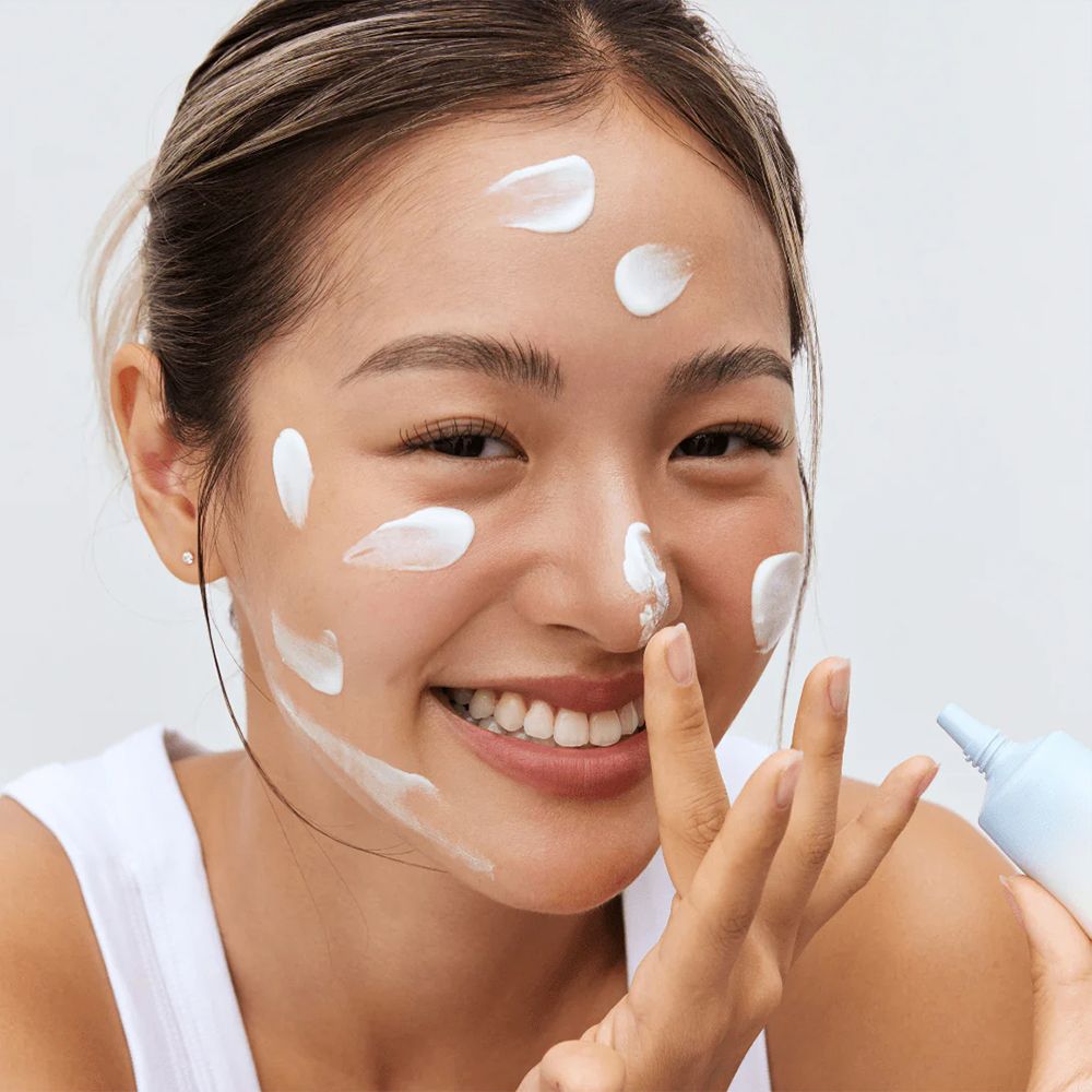 Donna applica crema solare bianca sul viso, tiene un tubetto.