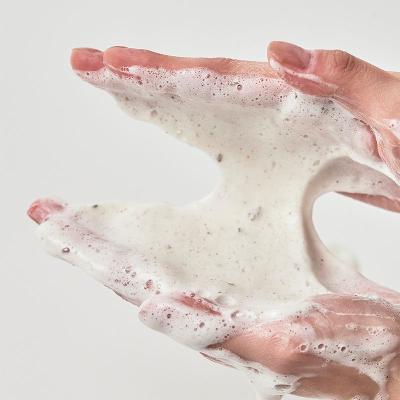 Mani con schiuma. Schiuma con piccole particelle. Sfondo bianco. Nessuna denominazione del prodotto visibile.