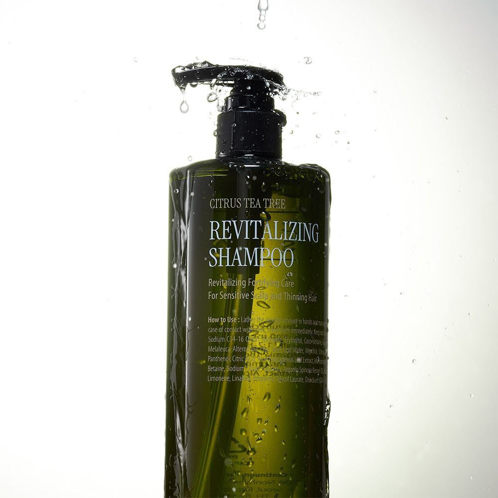 Flacone di shampoo verde con dosatore nero. L'acqua schizza sul flacone. Scritta: Revitalizing Shampoo.