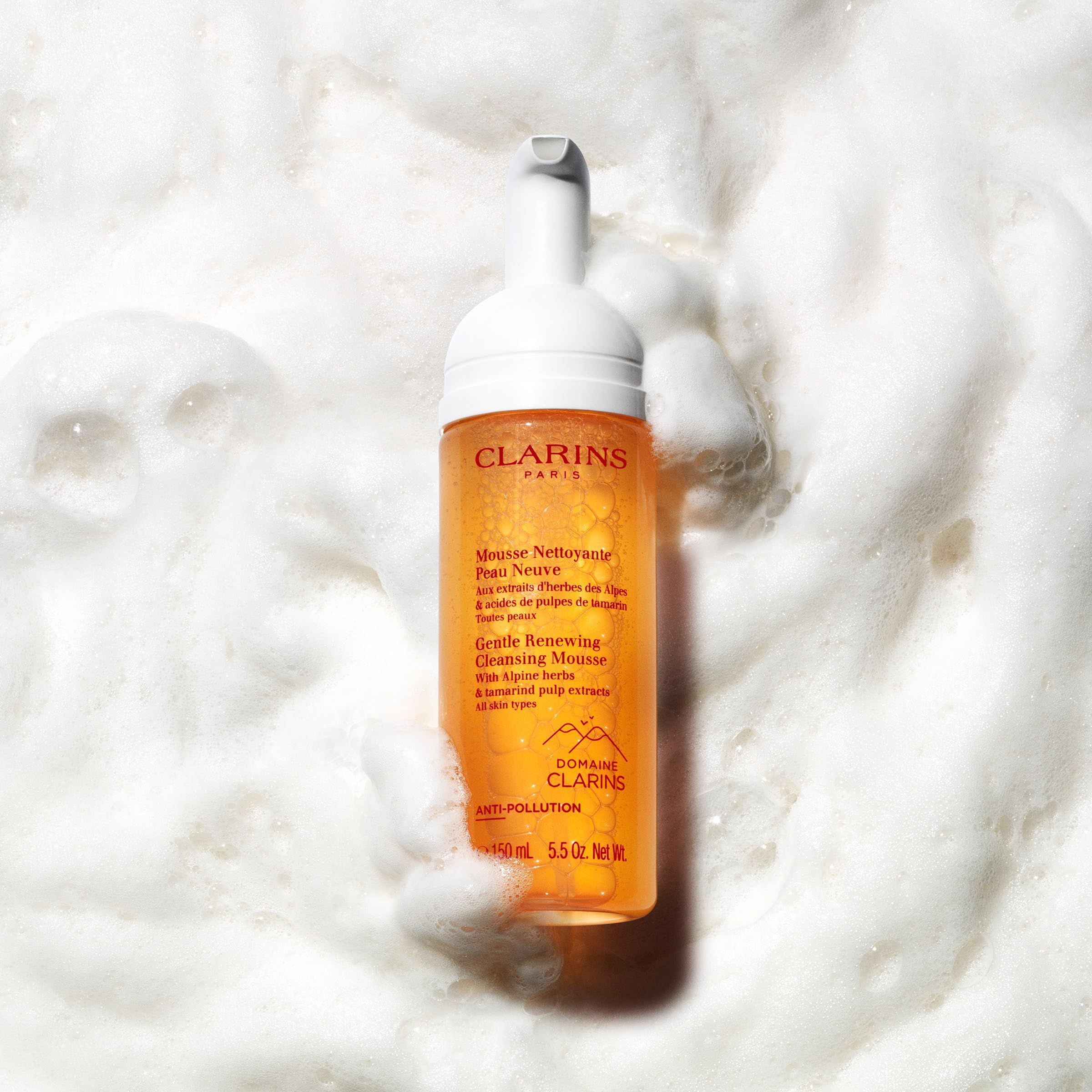 Flacone Clarins Mousse Detergente Delicata nella schiuma. Testo: Mousse Nettoyante Peau Neuve, Gentle Renewing Cleansing Mousse. Sfondo schiumoso.
