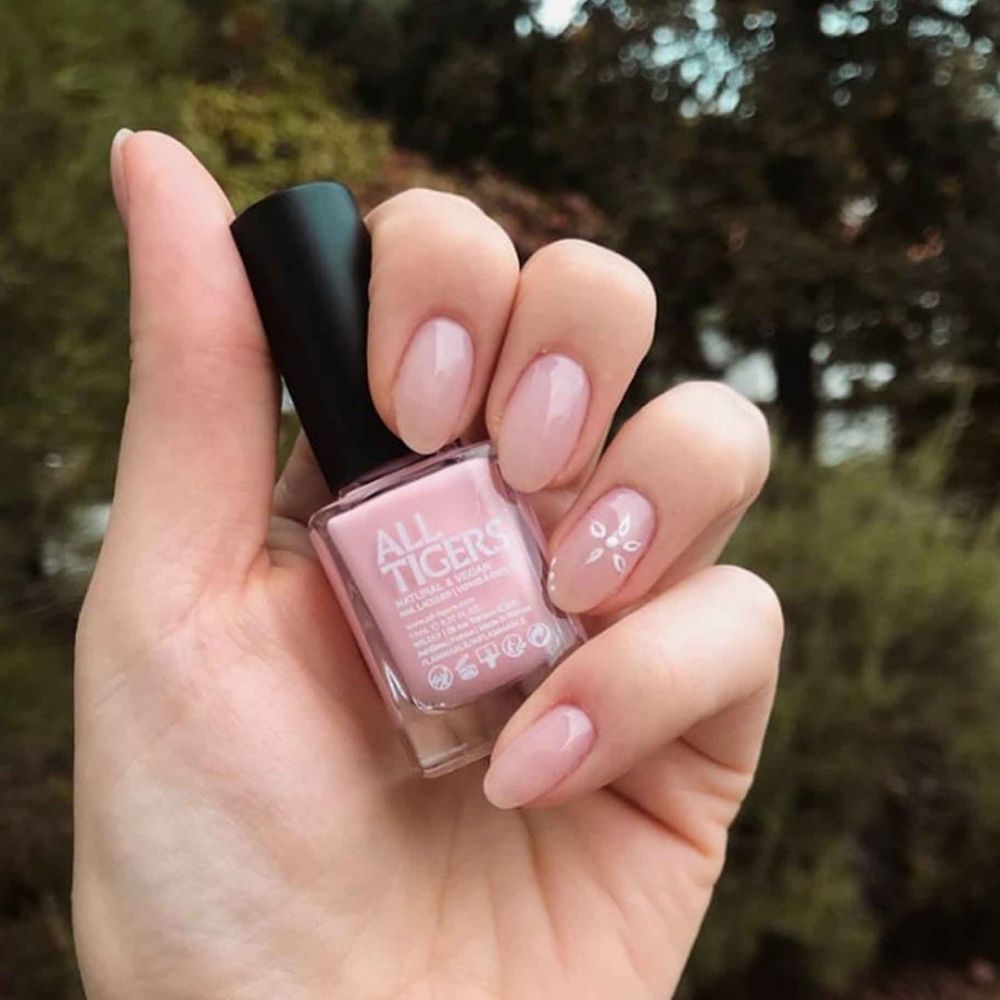 Mano che tiene un flacone di smalto. "ALL TIGERS" è scritto sul flacone. Unghie smaltate di rosa.
