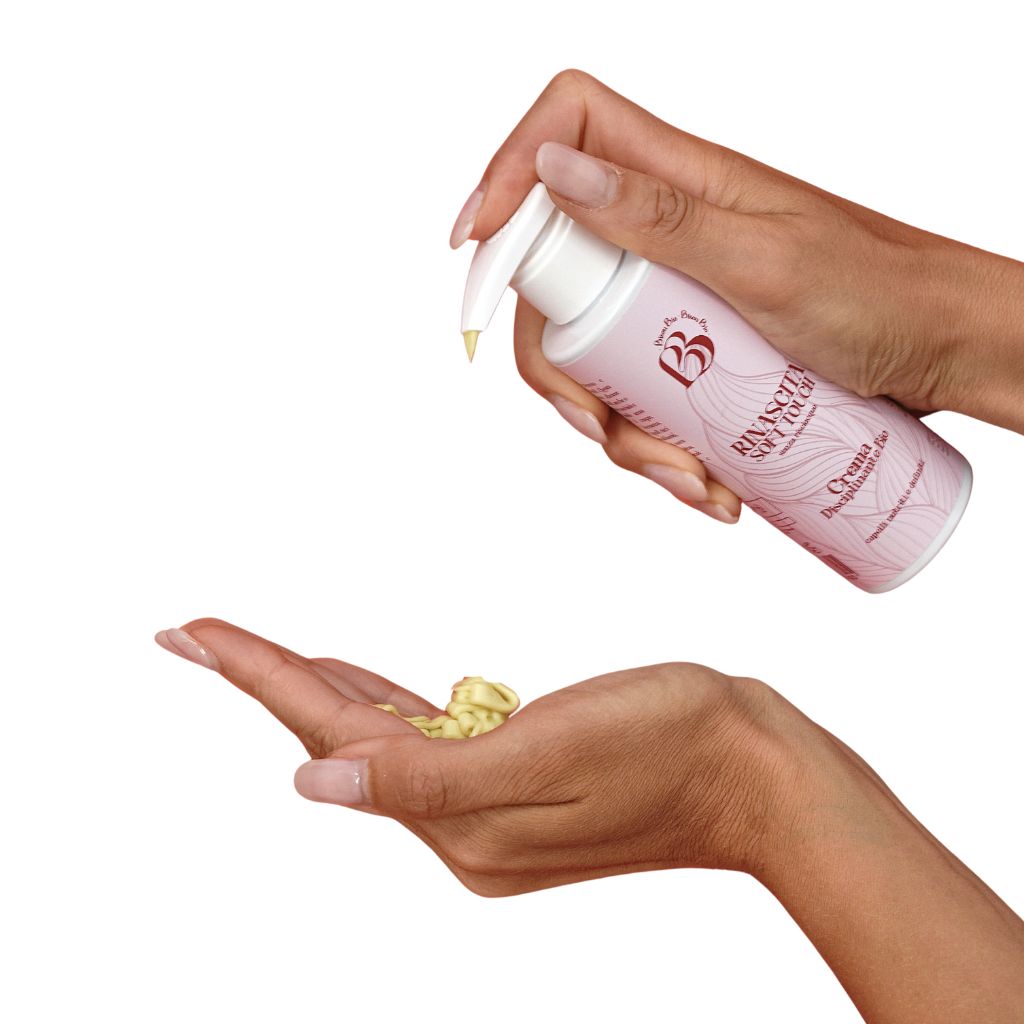 Mani che tengono flacone rosa con dosatore. Crema erogata nel palmo.