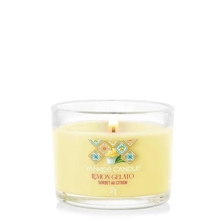 Candela gialla in vetro. Scritta: Lemon Gelato, 37g. Con fiamma. Etichetta decorativa con motivi floreali.