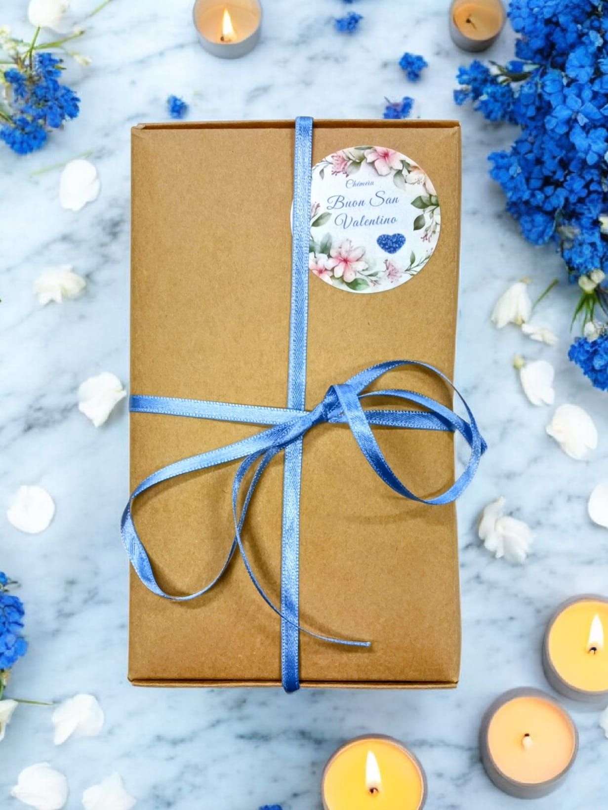 Scatola rettangolare marrone con nastro blu e adesivo rotondo. Adesivo con design floreale e testo.