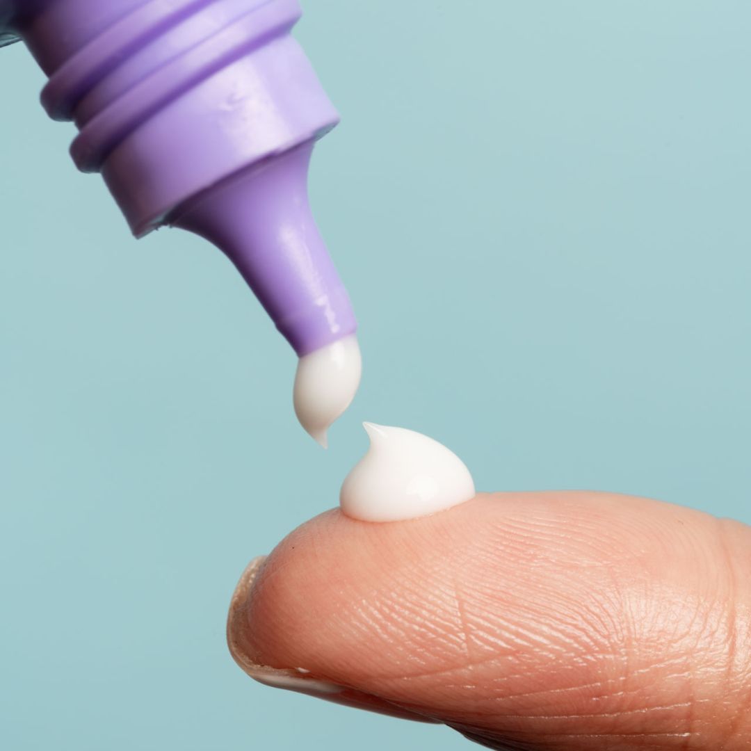 Crema spremuta da un tubo lilla su un dito. La goccia di crema è bianca.