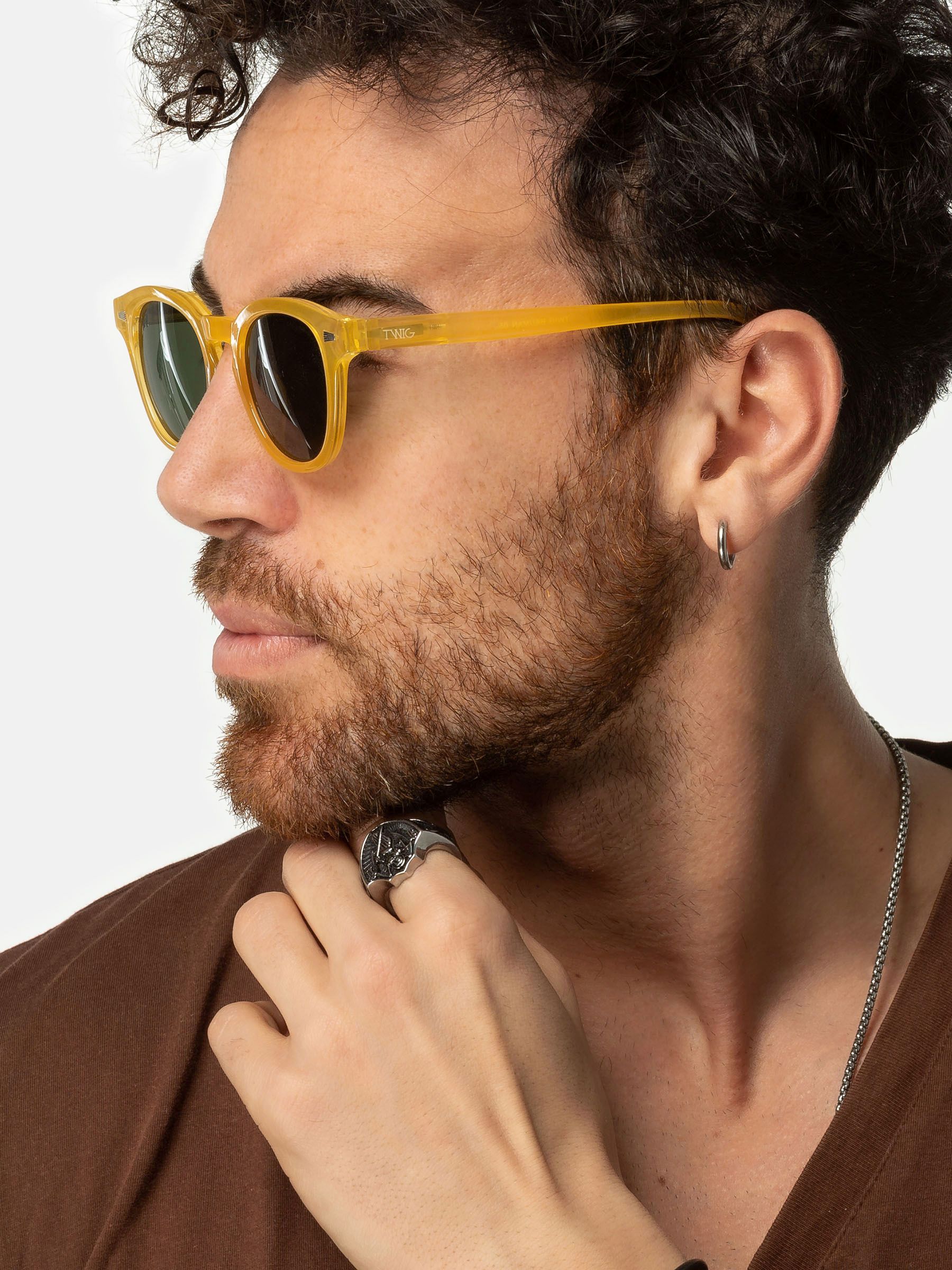 Uomo con occhiali da sole gialli. Primo piano. Anello e collana visibili.