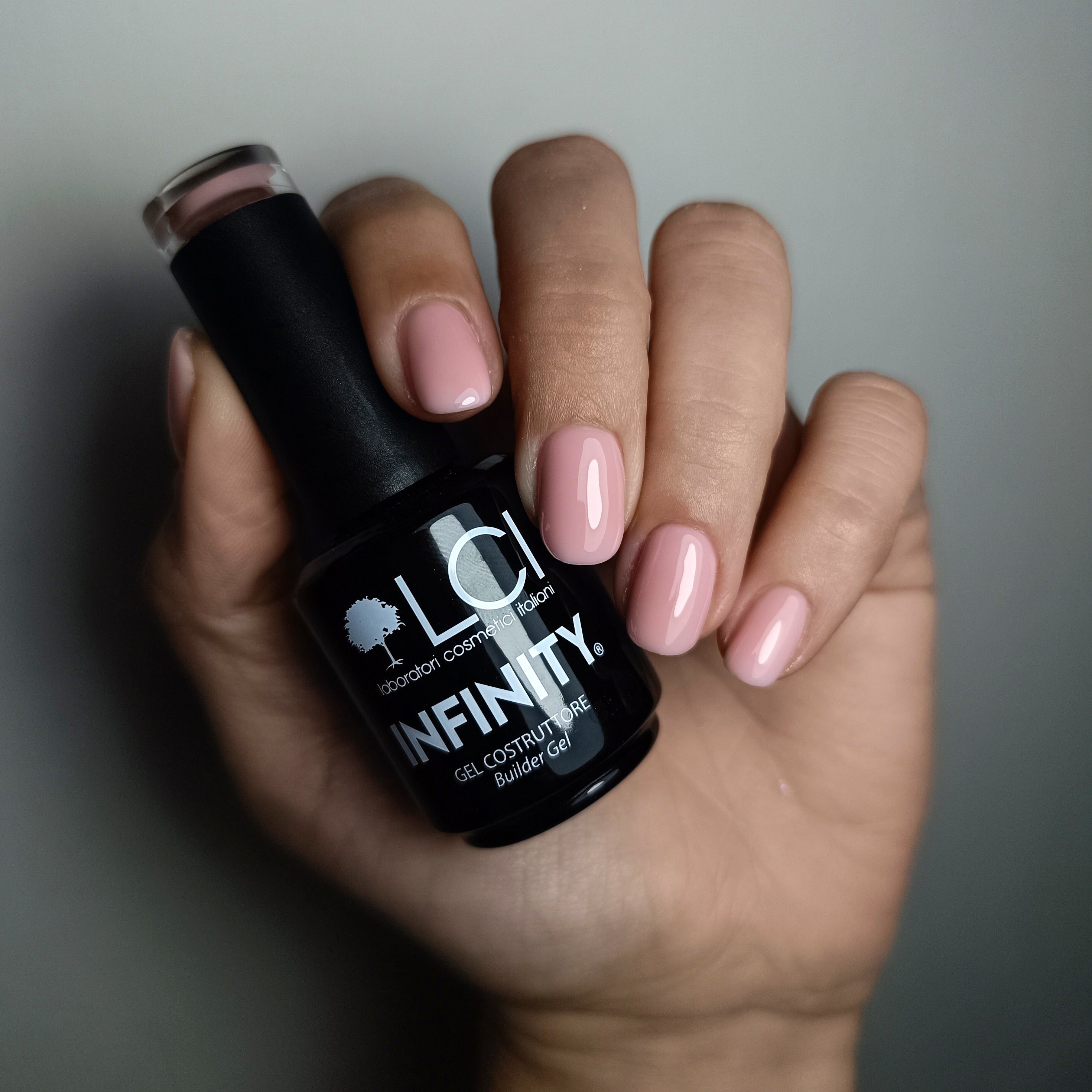 Mano che tiene un flacone di gel nude-rosa. Unghie smaltate nude-rosa.