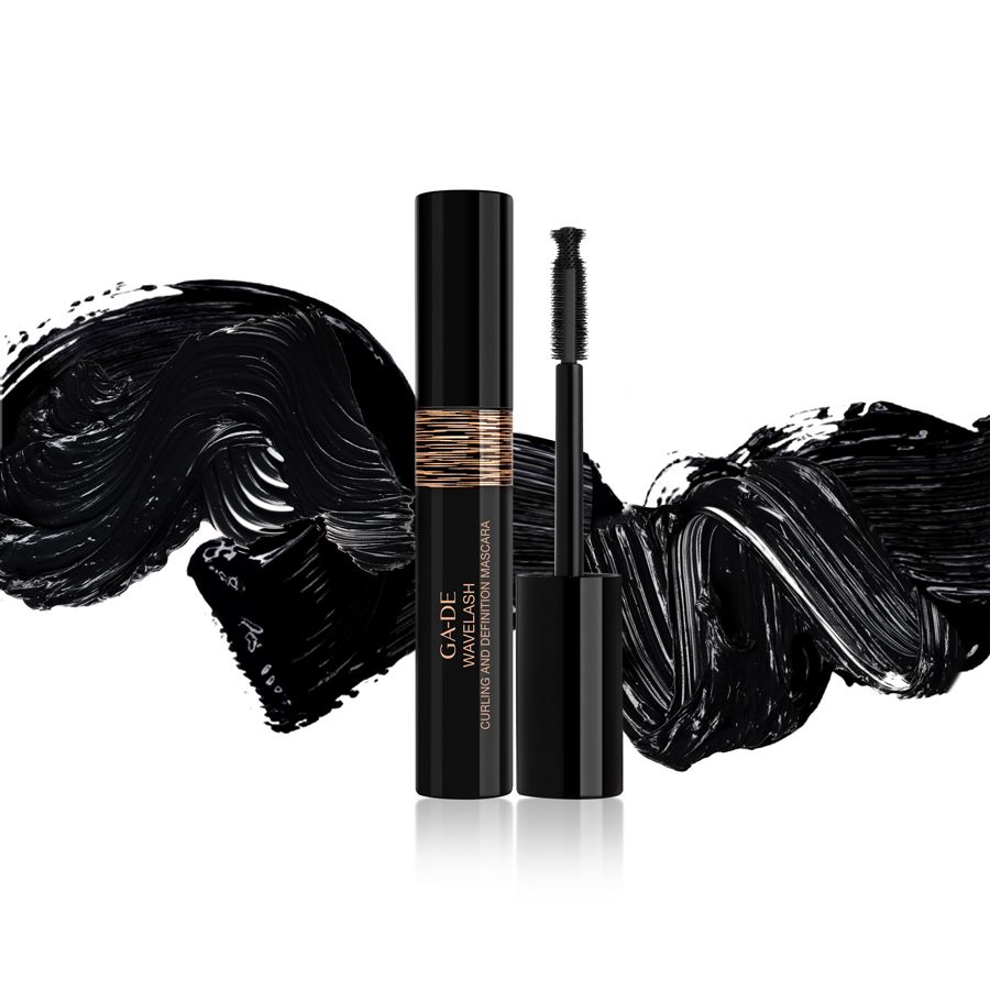 Tubo e spazzola di mascara nero. Fascia dorata con testo. Tracce di mascara nero sullo sfondo.