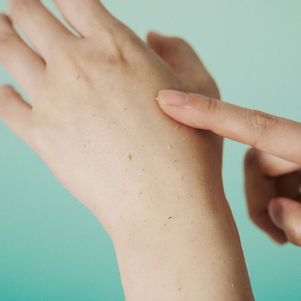 Mano con residui di peeling. Dito che tocca la pelle. Pelle chiara con piccole particelle.