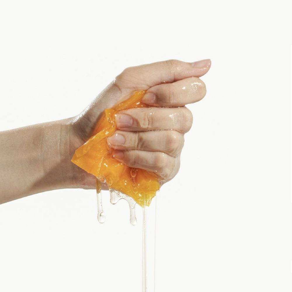 Mano che strizza un panno maschera giallo imbevuto. Liquido che cola. Sfondo bianco.