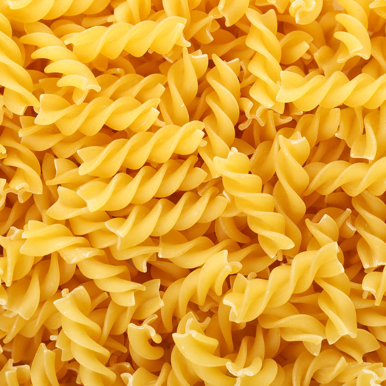 Primo piano di pasta fusilli cruda. Pasta a spirale giallastra, consistenza visibile.