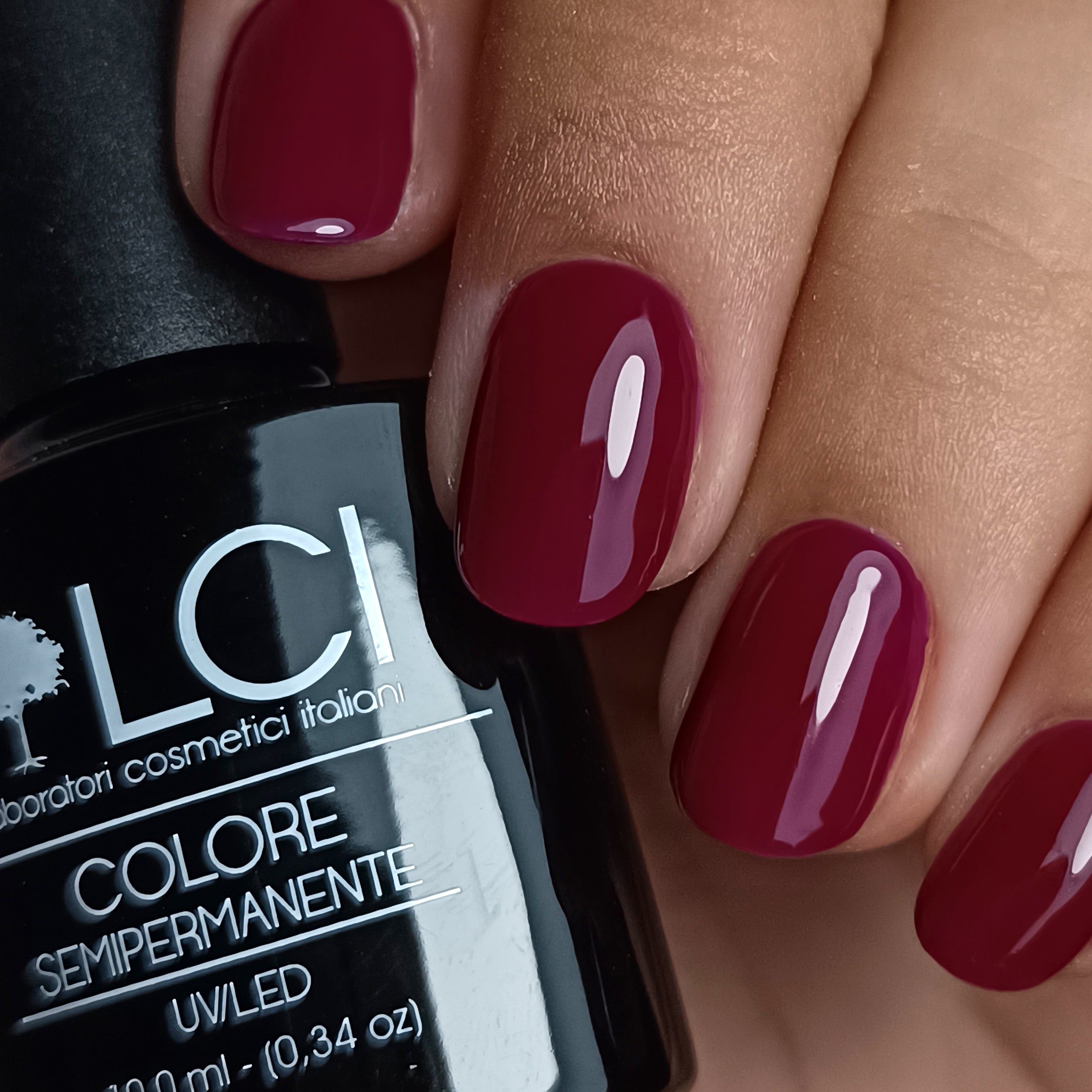 Mano con unghie laccate bordeaux. Flacone smalto con scritta LCI.