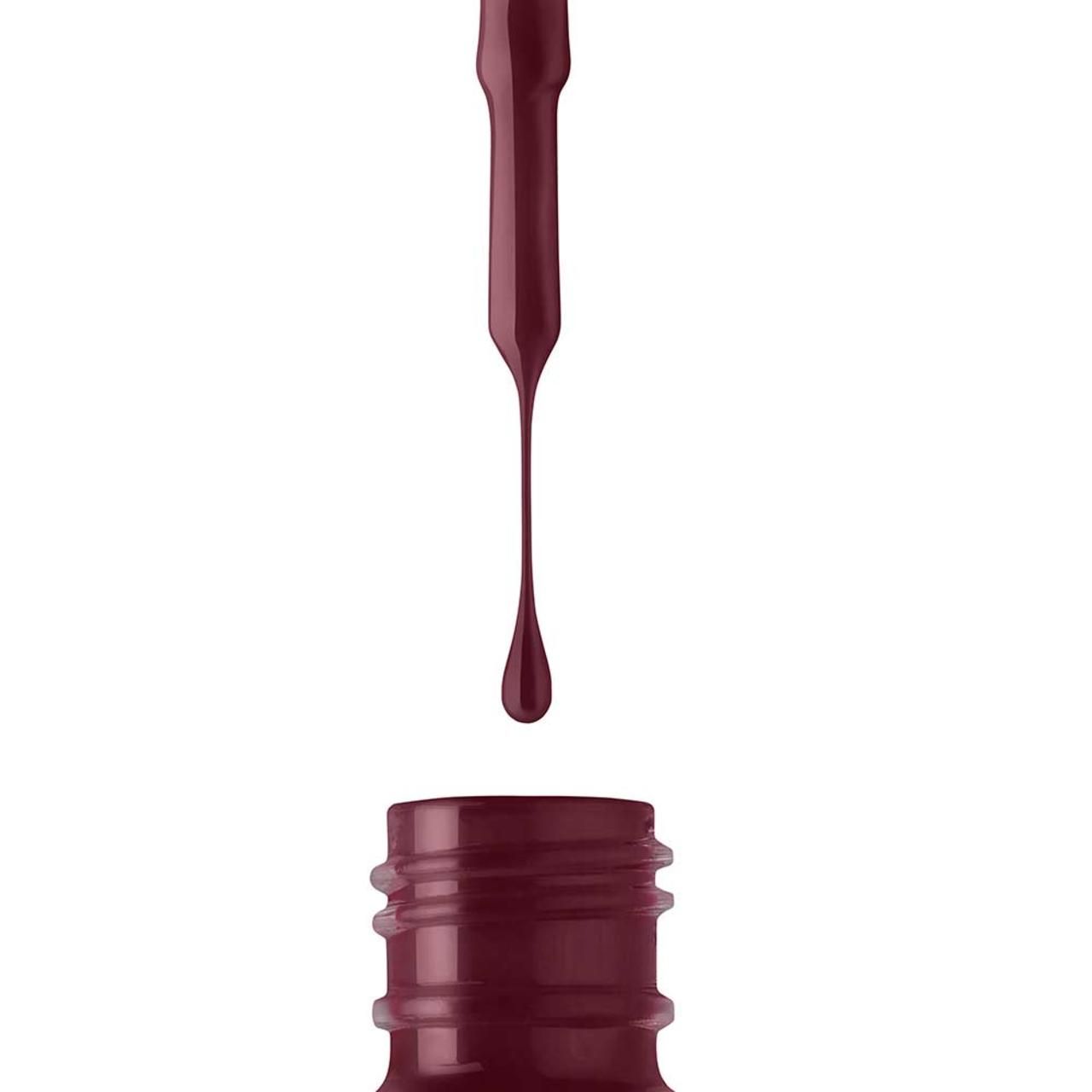 Primo piano di un flacone di smalto per unghie. Il pennello gocciola smalto. Lo smalto è rosso scuro.