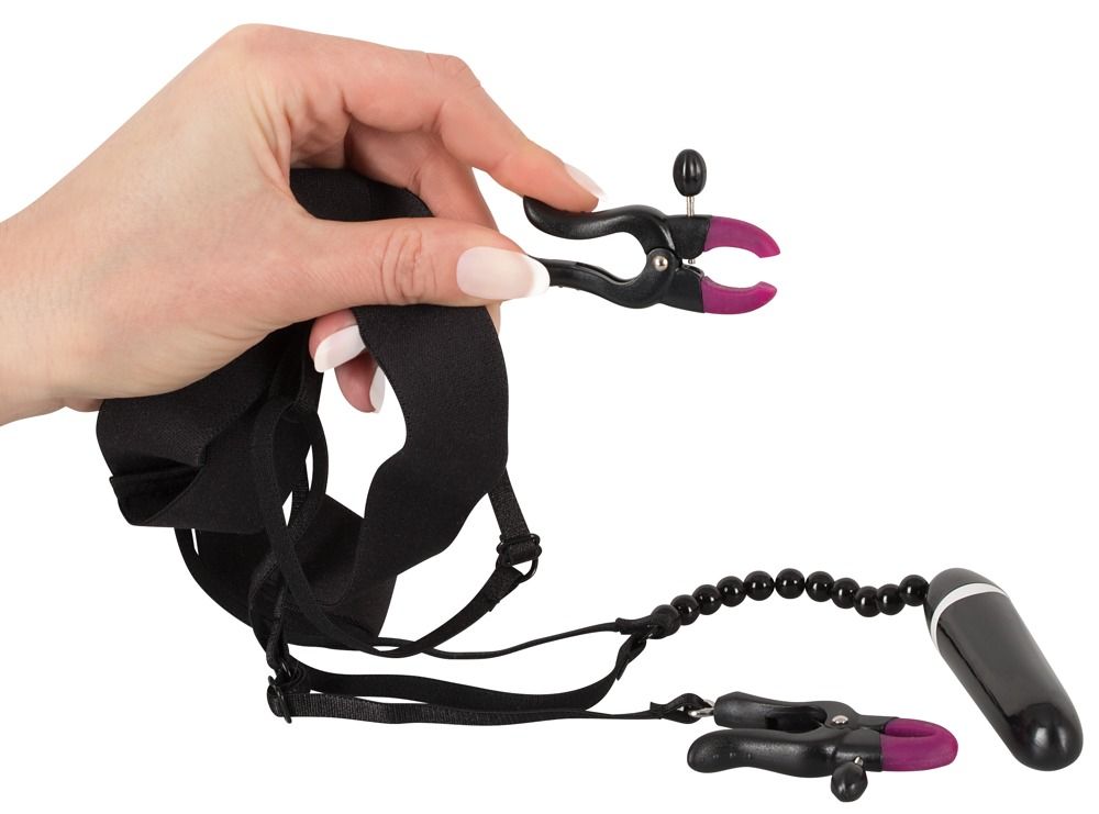 Mano che tiene una pinza per labbra. Pinza nera con accento rosa. String con catena di perle e vibratore. Fascia nera.